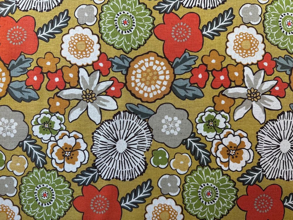 The image is a close-up of a fabric with a repeating pattern of various colorful flowers and leaves in shades of red, green, white, and gray.