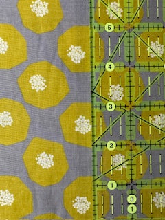 a fabric with a yellow and green floral pattern, and a ruler with numbered lines for measuring.
